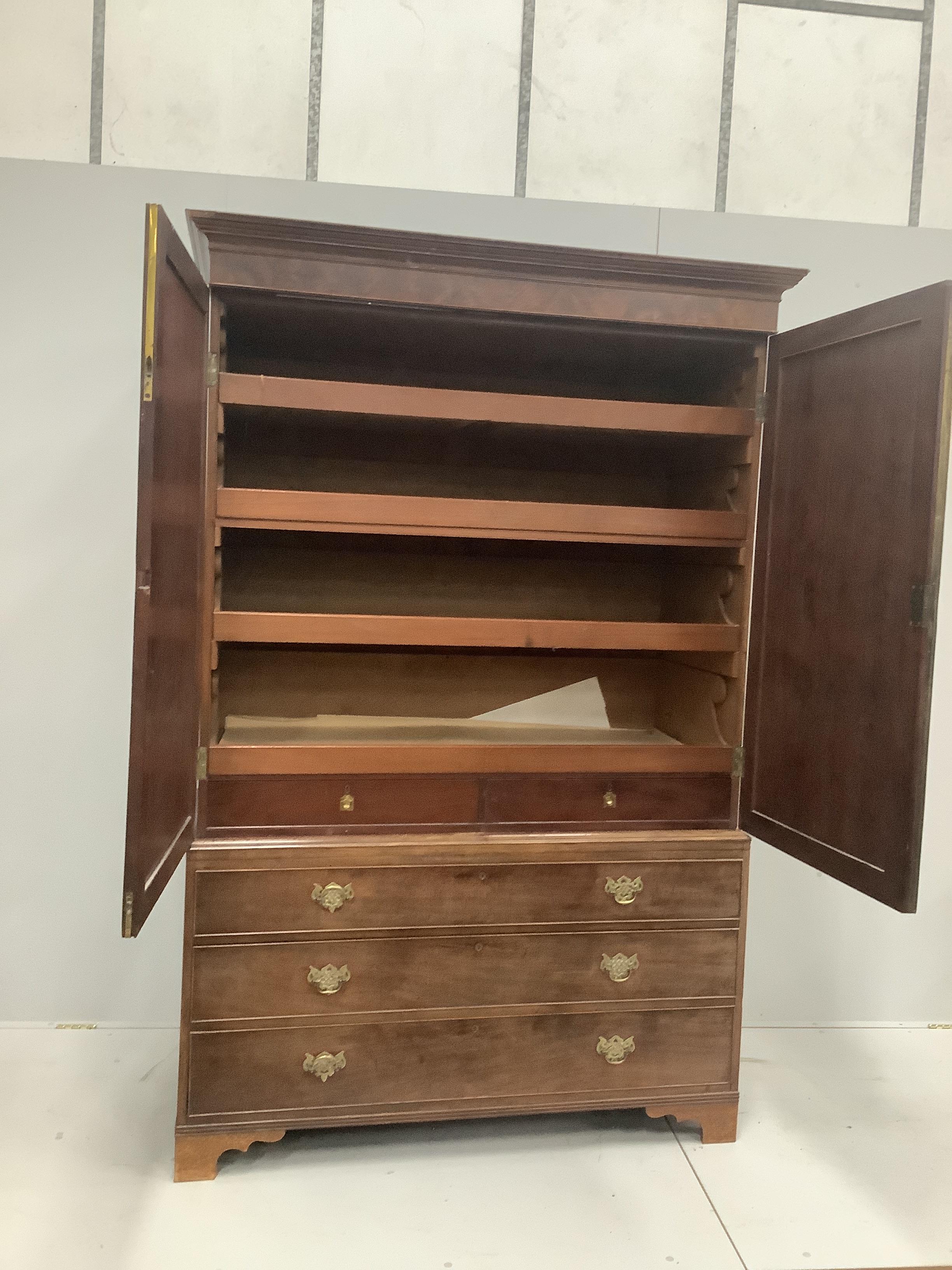 A George III mahogany linen press with moulded cornice and panelled doors enclosing sliding trays over three long drawers on bracket feet, width 137cm, height 195cm